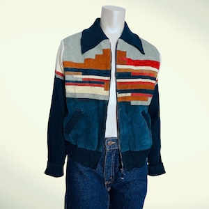 Puede incluir: Chaqueta vintage con diseño de bloques de color. La chaqueta presenta un cuello, mangas y sección inferior azul marino. La sección superior tiene un patrón geométrico en tonos grises, naranjas, rojos y blancos. La chaqueta está con cremallera.