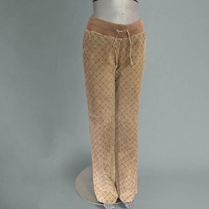 Puede incluir: Pantalones color beige con cintura con cordón y una superposición con estampado de diamantes. Los pantalones se exhiben en un maniquí sobre un fondo neutro. Los pantalones tienen un corte holgado y un estilo informal.