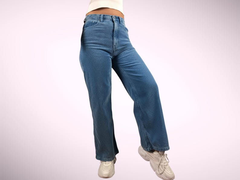 May include: Light blue denim jeans with a high waist and a wide leg. The jeans are worn with white sneakers. The overall style is casual and relaxed. The jeans are made of a durable denim material.