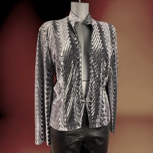 Puede incluir: Chaqueta plateada y negra estampada con un diseño de ondas único. La chaqueta tiene mangas largas y cuello. La chaqueta está abierta por delante y se exhibe en un maniquí. La chaqueta se combina con pantalones de cuero negros.