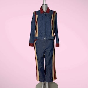 May include: A denim jacket and matching trousers set. The jacket features a burgundy collar and trim, with tan and burgundy stripes down the sleeves. The trousers have matching side stripes. The outfit is displayed on a mannequin.