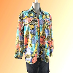 May include: A button-down shirt with a vibrant pop art print. The shirt features a collage of comic book-style women's faces, cars, and other graphics in shades of blue, yellow, orange, and black. The shirt has long sleeves and two chest pockets.
