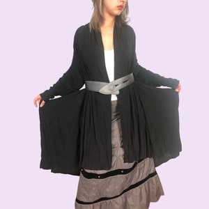 May include: A long, black, flowing cardigan with a wide, gray leather belt with a silver buckle. The cardigan is worn over a white tank top and a gray skirt.