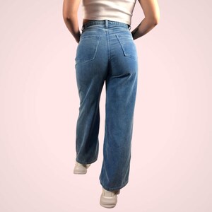 May include: Light blue corduroy pants with a high waist and a wide leg. The pants have two back pockets and a classic five-pocket design. The model is wearing a white top and white sneakers. The pants are made of a soft, textured fabric.