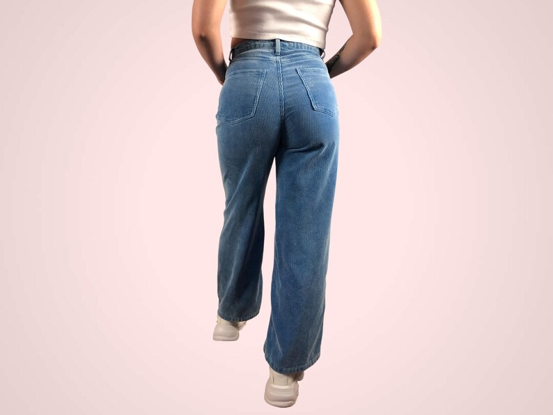 May include: Light blue corduroy pants with a high waist and a wide leg. The pants have two back pockets and a classic five-pocket design. The model is wearing a white top and white sneakers. The pants are made of a soft, textured fabric.