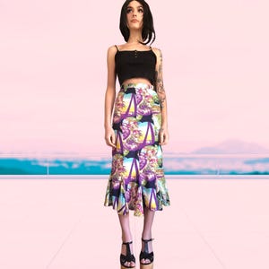 May include: A black crop top with thin straps and a knee-length skirt. The skirt has a tropical print with palm trees, purple and yellow details, and a flared hem. The model is wearing black heels. The skirt length is approximately 76 cm.