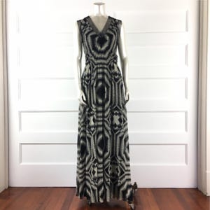 May include: A sleeveless, floor-length dress with a V-neckline. The dress features a black and white geometric pattern. The dress is displayed on a mannequin in front of a white door.