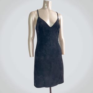 May include: A black suede mini dress featuring a V-neckline and thin spaghetti straps. The garment has a fitted silhouette that falls above the knee, showcasing a soft, matte texture throughout the entire surface of the sleeveless piece.