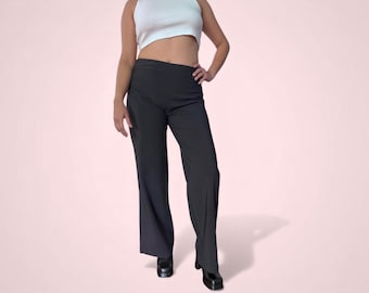 Peut inclure: Pantalon noir taille haute à jambes larges. Le pantalon est associé à un crop top blanc et des chaussures noires. La tenue est présentée sur un fond rose clair.