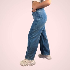 May include: Light blue corduroy pants with a straight leg design. The pants have a classic five-pocket style and are worn with white sneakers. The corduroy fabric has a subtle texture, and the pants are a medium wash.
