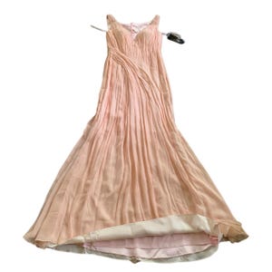 Puede incluir: Un vestido de noche rosa p&aacute;lido con una falda fluida y plisada y un corpi&ntilde;o ajustado. El vestido presenta delicadas correas para los hombros y un escote en V. La tela del vestido parece ligera y tiene un brillo sutil, adecuado para ocasiones especiales.