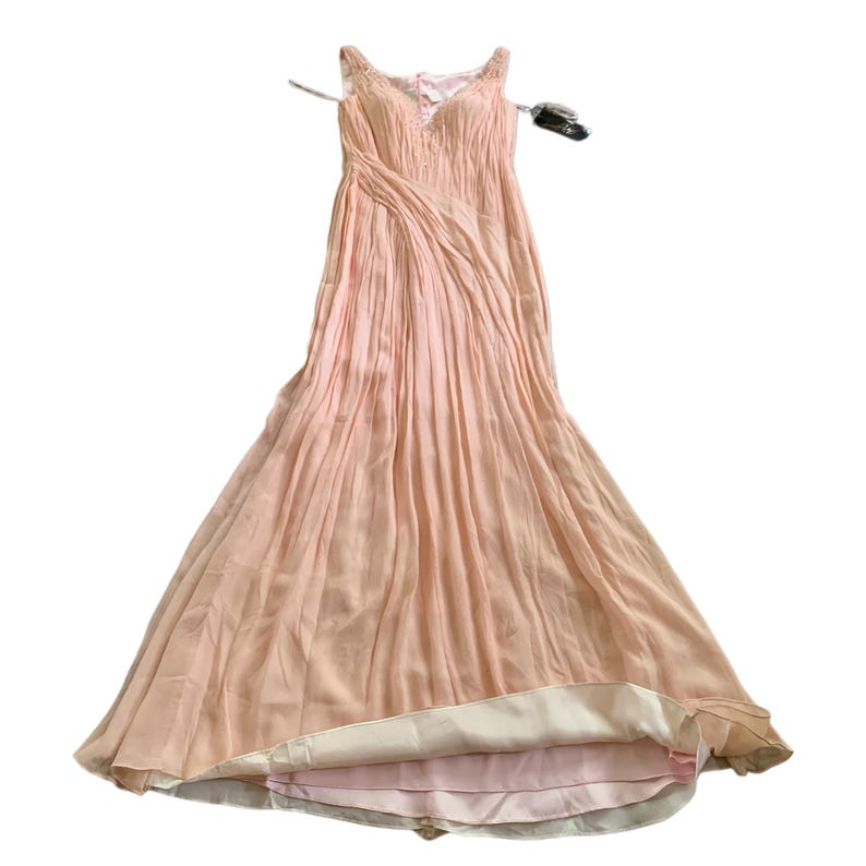 Puede incluir: Un vestido de noche rosa p&aacute;lido con una falda fluida y plisada y un corpi&ntilde;o ajustado. El vestido presenta delicadas correas para los hombros y un escote en V. La tela del vestido parece ligera y tiene un brillo sutil, adecuado para ocasiones especiales.