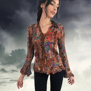 May include: A brown, long-sleeved blouse with a V-neck and flared sleeves. The blouse features a textured, crinkled fabric with a colourful, abstract pattern in shades of red, blue, green, and orange. The collar and cuffs have a leopard print.