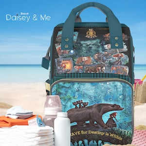 May include: A teal blue diaper bag with a plaid pattern and a print of a bear and a girl with a bow and arrow. The bag has a zippered pocket and a handle. The text "Brave for Destiny is Within" is printed on the bag.