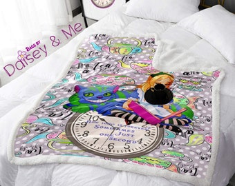 May include: A purple and white fleece blanket with a whimsical Alice in Wonderland theme. The blanket features a cartoon illustration of Alice holding a book, the Cheshire Cat, and a teapot with the text "It's a Tea Party". The blanket also features a clock with the text "How long is forever? Sometimes just one second."