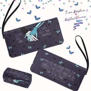 May include: A purple wallet with a black wrist strap features a graphic of two hands holding each other. The text "With this hand I will lift your sorrows" is printed on the wallet. The wallet is decorated with a repeating pattern of small hearts and butterflies.