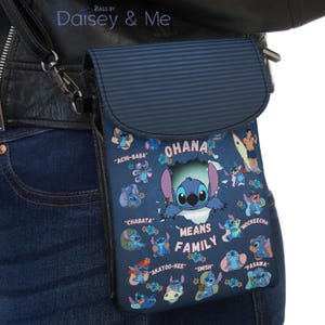 May include: A blue crossbody bag featuring a cartoon character design with the text "OHANA MEANS FAMILY". The bag has a flap closure and a striped pattern on the flap. The bag is worn across the body.
