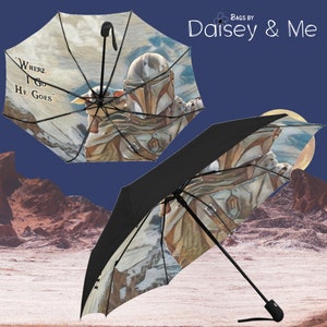 May include: A black and white umbrella with a colorful image of a Mandalorian character and a small creature. The umbrella has a black handle and the text "Where I Go He Goes" is printed on the umbrella.