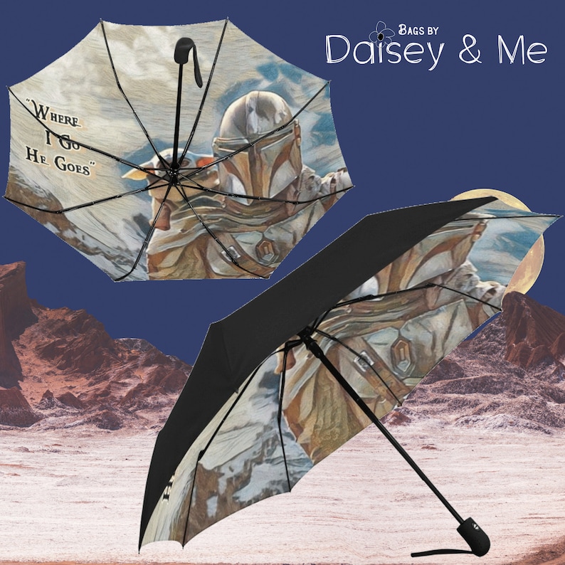 May include: A black and white umbrella with a colorful image of a Mandalorian character and a small creature. The umbrella has a black handle and the text "Where I Go He Goes" is printed on the umbrella.