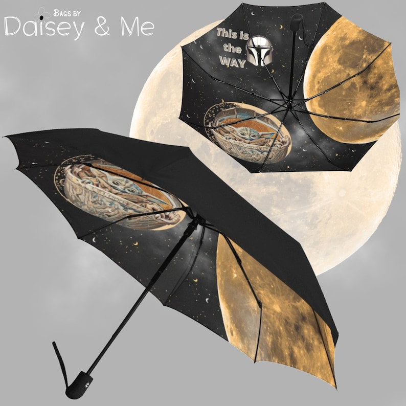 May include: A black umbrella with a yellow moon and stars printed on it. The umbrella also features a character from the Star Wars franchise, Grogu, in a spaceship. The text "This is the WAY" is printed on the umbrella.