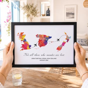 Op de afbeelding: Een ingelijste print met aquarelkaarten van Groot-Brittannië, Spanje en Nieuw-Zeeland, verbonden door stippellijnen met vliegtuigjes. De tekst luidt: Not all those who wander are lost, GREAT BRITAIN | SPAIN | NEW ZEALAND, AUGUST 2024.