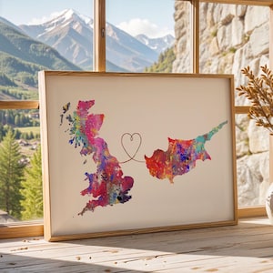 Puede incluir: Una impresión en acuarela enmarcada que presenta los mapas de Gran Bretaña y Chipre, conectados por un corazón. Los mapas están llenos de colores vibrantes, incluyendo rosa, azul y amarillo. El marco es de madera clara.