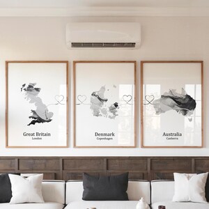 Könnte beinhalten: Drei gerahmte Kunstdrucke mit Graustufen-Aquarellkarten von Großbritannien, Dänemark und Australien. Jeder Druck enthält den Ländernamen und die Hauptstadt, verbunden durch ein herzförmiges Band. Die Rahmen sind hellbraun.