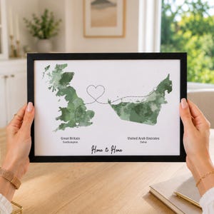 May include: A framed print featuring a white background with watercolour-style green maps of Great Britain and the United Arab Emirates. A dotted line connects the two regions in a heart shape. Text reads Great Britain, Southampton, United Arab Emirates, Dubai, and Home to Home.