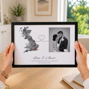 Puede incluir: Una impresión enmarcada con un mapa en acuarela del Reino Unido, un punto rojo y una línea en forma de corazón que conecta con una foto en blanco y negro de una pareja. El texto dice Lina & Amar, ONE WHITEHALL PLACE, LONDON, 24 AUGUST 2023.