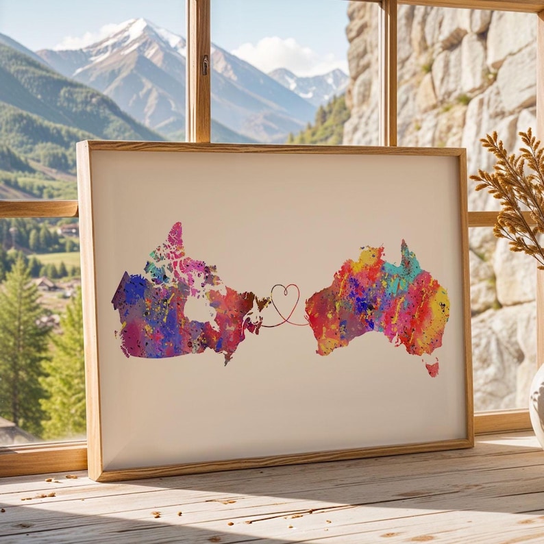 May include: A framed print featuring watercolor maps of Canada and Australia, connected by a heart-shaped line. The maps are filled with vibrant colors, including pink, blue, yellow, and red, set against a cream background.