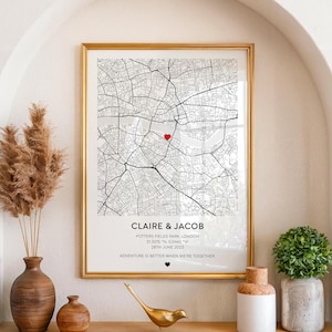 May include: A framed map print with a gold border. The black and white map features a red heart marking a location. Text at the bottom reads "CLAIRE & JACOB" and "ADVENTURE IS BETTER WHEN WE'RE TOGETHER."