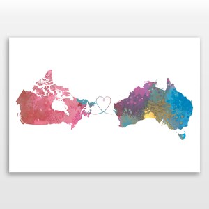 May include: Watercolor print featuring the maps of Canada and Australia connected by a heart-shaped line. The Canada map is pink and red, while the Australia map is blue, purple, and yellow. The artwork is on a white background.