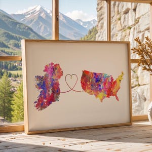 Può includere: Stampa artistica incorniciata con mappe ad acquerello di Irlanda e Stati Uniti, collegate da un cuore. Le mappe sono piene di colori vivaci, su sfondo crema e incorniciate in legno chiaro.