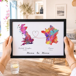 Könnte beinhalten: Ein gerahmter Druck mit Aquarellkarten von Großbritannien und Frankreich, verbunden durch eine herzförmige Linie. Die Karten sind mit leuchtenden Farben gefüllt. Der Text unten lautet "Home to Home."