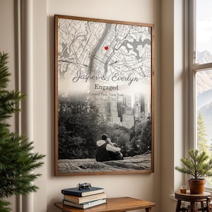 Könnte beinhalten: Schwarzweißfoto eines Paares, das sich in Central Park, New York City, umarmt. Das Foto ist mit einer Karte der Stadt überlagert, wobei ein rotes Herz die Lage des Central Parks markiert. Der Text "Jasper & Evelyn Verlobt Central Park, New York 5. August 2021" ist unter der Karte gedruckt.