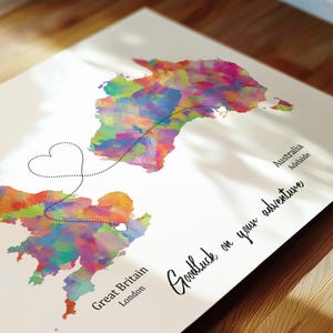May include: A watercolor map print featuring Great Britain and Australia, connected by a dotted line with a heart shape. The map is filled with vibrant colors, including pink, blue, and yellow. Text reads "Goodluck on your adventure."