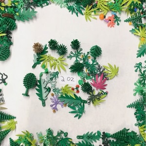 May include: A collection of green, red, and purple plastic LEGO pieces shaped like leaves, flowers, and trees. The pieces are arranged on a white surface with a handwritten label that says "2 oz".