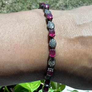 May include: A silver bracelet featuring alternating oval and pear-shaped gemstones. The oval stones are a vibrant pink, while the pear-shaped stones are encrusted with small, sparkling accents. The bracelet is displayed on a wrist.
