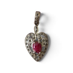 May include: A heart-shaped pendant crafted from silver-toned metal, featuring a central oval-cut deep pink gemstone. The frame is decorated with small, clear pavé-set stones, and the bail at the top is also embellished with matching clear stones.
