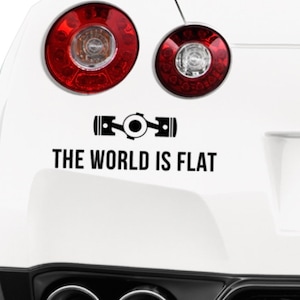 Può includere: Un'auto bianca con un adesivo nero sul paraurti che dice "The World Is Flat" con un'immagine stilizzata di un albero a gomiti sopra il testo.