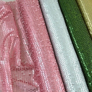 Peut inclure: Gros plan sur plusieurs rouleaux de tissu à paillettes de différentes couleurs. Les couleurs comprennent le rose, le blanc, le vert et l'or. Le tissu est densément recouvert de petites paillettes rondes, créant un effet scintillant.