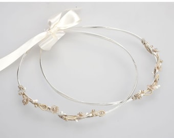 May include: Two silver wedding crowns with delicate floral designs and white ribbon.