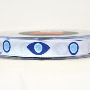 May include: A spool of white ribbon with a repeating pattern of blue evil eye symbols. The ribbon is made of a smooth, satin-like material and is ideal for crafting or gift wrapping.