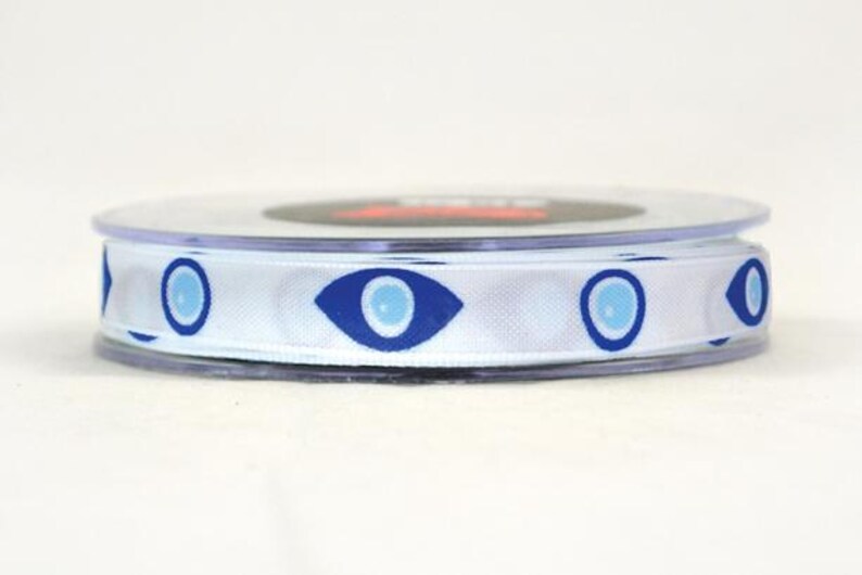 May include: A spool of white ribbon with a repeating pattern of blue evil eye symbols. The ribbon is made of a smooth, satin-like material and is ideal for crafting or gift wrapping.