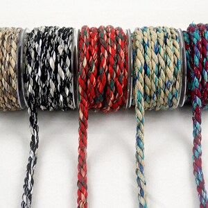 Op de afbeelding: Vijf spoelen gevlochten koord in verschillende kleuren. De koorden zijn in tinten beige, zwart en wit, rood en groen, beige en blauw en bordeaux en blauwgroen. Elke spoel is gemaakt van een strak geweven, getextureerd materiaal.