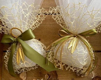 May include: Two white tulle favor bags with gold leaf accents and green satin ribbon bows. The bags are filled with small, dried flower petals and are sitting on a wooden surface.