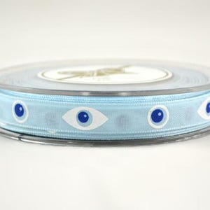 May include: A spool of light blue ribbon with a repeating pattern of white and blue eye designs. The ribbon is contained in a clear plastic spool with a white label.