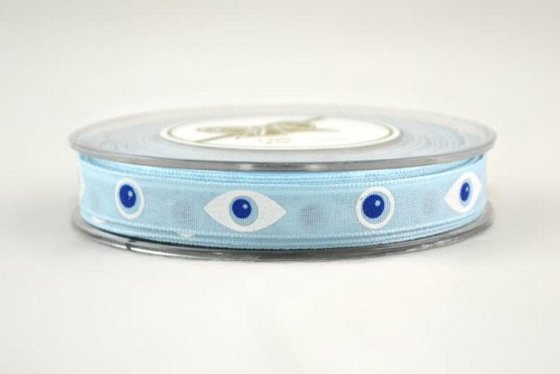 May include: A spool of light blue ribbon with a repeating pattern of white and blue eye designs. The ribbon is contained in a clear plastic spool with a white label.