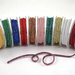 May include: A collection of 12 spools of metallic glitter ribbon in various colours, including gold, silver, red, green, blue, and pink. The ribbon is wound around spools with clear plastic cases.