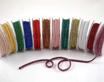 May include: A collection of 12 spools of metallic glitter ribbon in various colors, including gold, silver, red, green, blue, and pink. The ribbon is wound around spools with clear plastic cases.